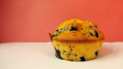A blueberry muffin made from pea flour, rice flour, eggs, dark chocolate and yogurt sits on a white surface with a side view of a red wall . homemade cakes