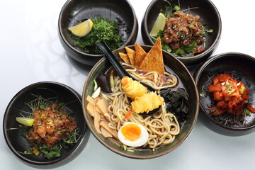 A composition of: ramen with shrimps, tuna, salmon tartare, kimchi, pickled seagrass Japanese salad, isolated on white.