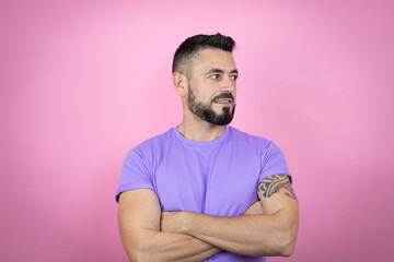 Young handsome man wearing casual t-shirt over pink background looking to the side with arms crossed convinced and confident