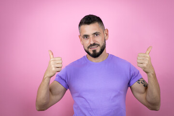 Fototapeta premium Young handsome man wearing casual t-shirt over pink background success sign doing positive gesture with hand, thumbs up smiling and happy. cheerful expression and winner gesture.