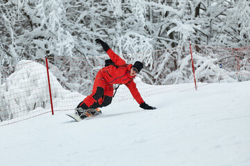 Male snowboarder in a red suit rides on the snowy hill with snowboard, Skiing and snowboarding...
