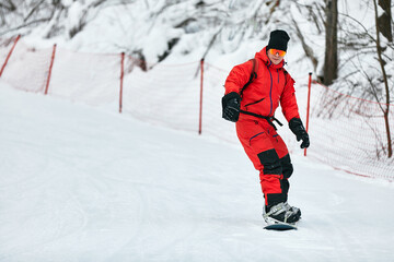 Fototapeta na wymiar Male snowboarder in a red suit rides on the snowy hill with snowboard, Skiing and snowboarding concept