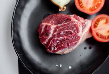 Food photo of beef on a black plate with tomatoes and onions. A juicy piece of meat and sea salt and pepper.