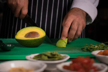 Chef cook preparing salad with salmon and avocado in his kitchen. Freezer food prepare in process vegetarian salad by chef hand in home kitchen. Dark black background with Text area for design menu 