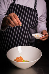 Chef cook preparing salad with salmon and avocado in his kitchen. Freezer food prepare in process vegetarian salad by chef hand in home kitchen. Dark black background with Text area for design menu 