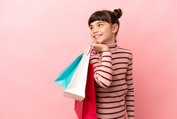 Little caucasian girl isolated on pink background holding shopping bags and looking back