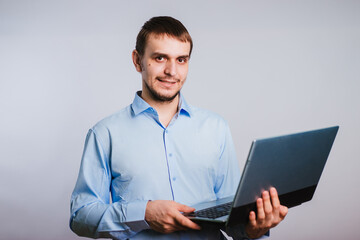 A guy in a blue shirt holds a laptop on a white background. Male office worker. Photo in studio