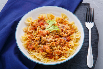 Pasta in tomato bolognese sauce on a round black stand on a blue napkin next to a fork