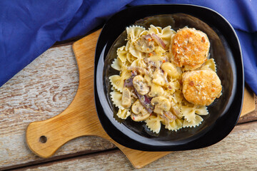 Pasta in a creamy sauce with mushrooms and chicken meatballs in a plate on a board on a blue napkin.