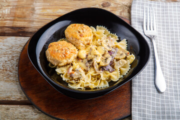Pasta in a creamy sauce with mushrooms and chicken meatballs in a black plate on a napkin next to a fork.