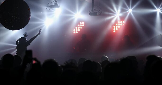 Silhouette of a Girl at a DJ Party Concert with Hands Outstretched on the Background of the Music Festival Scene and Light show. DNB Concert in Night Club. Dj on the scene stage.