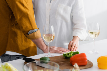 Cropped view of senior couple standing near glasses with wine and paprika on kitchen table