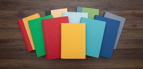 Top down view of a pile of bright colorful books centered on a dark desk.