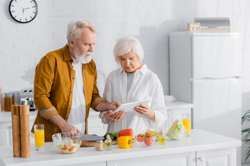 Senior couple using digital tablet while cooking in kitchen