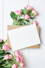 Greeting card with envelope and fresh roses on white background, mockup with copy space