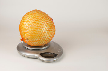 A ripe pomelo is packaged in a grid lies on scales over white background
