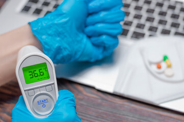 Doctor in medical gloves measures the temperature with an infrared thermometer. Medical concept.