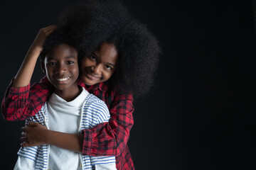 African teen siblings boy and girl hugging with smiley face on black background. Older sister hug...