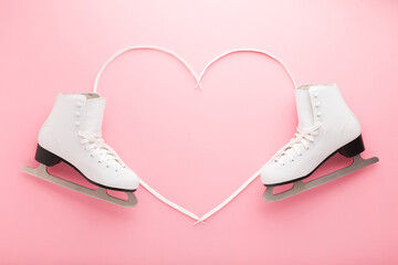 Heart shape created from shoelaces. White female figure skates on light pink table background....