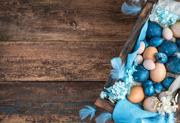 Easter background with marble blue and pastel quail and chicken eggs, decorated with blue feathers and flowers. Top view.