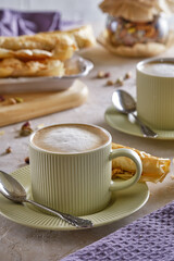 Fragrant cappuccino coffee with puff tubes with meringue and pistachios close-up
