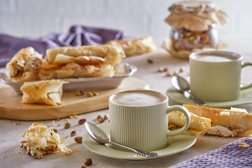 Fragrant cappuccino coffee with puff tubes with meringue and pistachios close-up
