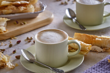 Fragrant cappuccino coffee with puff tubes with meringue and pistachios close-up