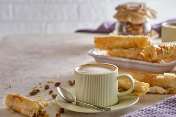 Fragrant cappuccino coffee with puff tubes with meringue and pistachios close-up