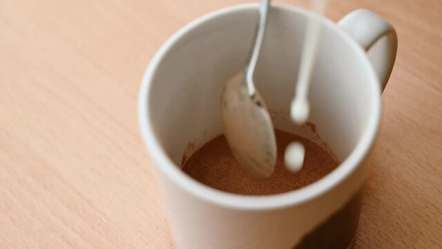 SLOW MOTION CLOSE UP looking into a mug as a teaspoon stirs milk as it's added to cocoa powder