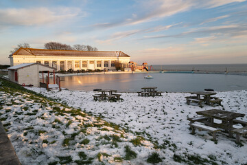 The boating pool building catching the sunset on a winter eveing. There is snow on the grass around...