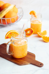 Homemade spring detox smoothie from oranges, carrots and banana in mason jar and glass straw