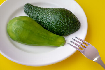 Avocado slices are on a plate. One slice is peeled. Yellow background