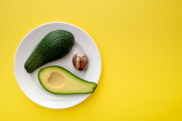 There are two slices of avocado on the plate. The fruit is divided into two parts. Next to it is an avocado seed. Yellow background color
