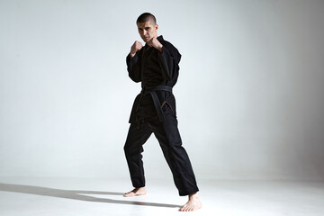 Angry guy trainer in black kimono fighter posing in karate stance on studio background with copy...