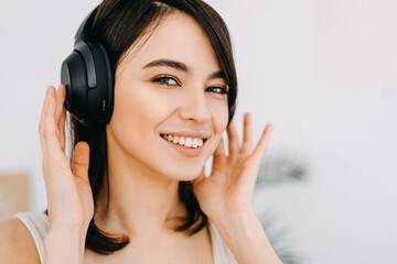 Closeup portrait of a young woman smiling, listening to music in wireless headphones.