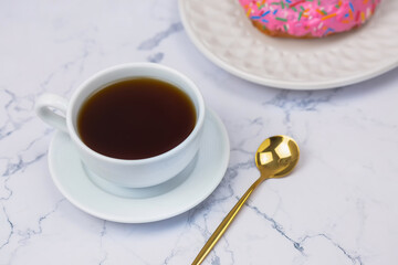 Cup of black coffee with pink donut on the white marble background
