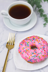 Cup of black coffee with pink donut on the white marble background