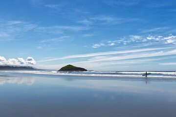 Surfer is walking with a White board along the Long Beach near Tofino, Vancouver Island, Canada at...