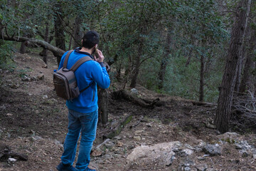 Fototapeta na wymiar Man lost in the deep forest, with a backpack, calling the emergency phone. 