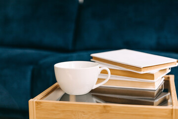 Blank white mug of coffee or tea on a table at home, next to few books.