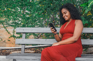 Young girl of Latin origin and dark skin sitting on a park bench with a gesture on her face and a...