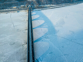 Aerial drone view. The shadow from the metro bridge in Kiev falls on the frozen Dnieper River. Sunny winter morning.