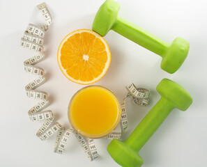 a glass of freshly squeezed orange juice and orange, a measuring tape and green dumbbells. White background. healthy lifestyle and proper nutrition, weight loss, diet. flat lay.