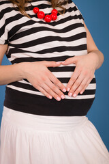 Perfect girl hugs her tummy while holding her hands in the shape of a heart. Waiting for a baby, pregnancy.