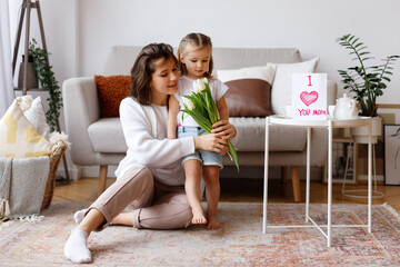 mom and daughter on holiday with flowers and a postcard at home in the living room
