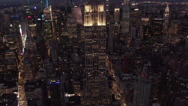 Slow tilt up revealing Empire State Building in Manhattan at Night surrounded by Skyscrapers in Big City Skyline, Aerial View forward