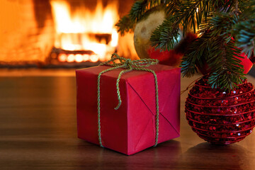 Fototapeta na wymiar Xmas tree branch with red balls, gift boxes, blur burning fireplace background.