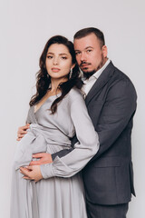 Pregnancy photoshoot of a beautiful couple, future parents in a gray dress and suit