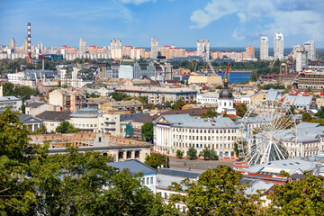 The landscape of summer Kyiv with a view of the old district of Podil with a Ferris wheel, old and new buildings and a new neighborhood on the horizon.