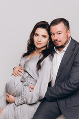Pregnancy photoshoot of a beautiful couple, future parents in a gray dress and suit